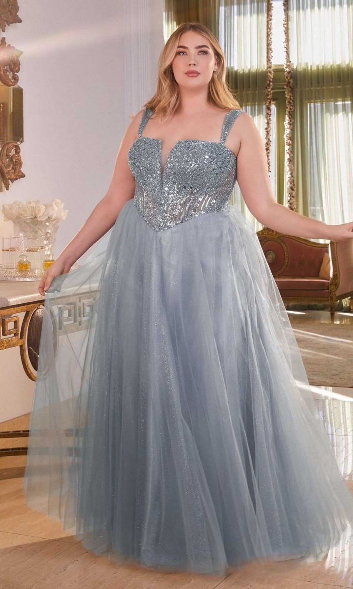 A woman wears the Plus-Size Sequin-Bodice Long Prom Dress CD0217C, sparkling in light blue as she stands in an elegant room with tall windows and ornate décor.
